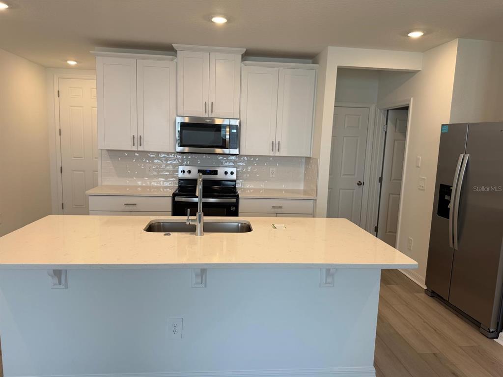 A modern kitchen features white cabinets, a quartz island with a sink, and stainless appliances — 4264 RANCH HOUSE ROAD, ST CLOUD, FL