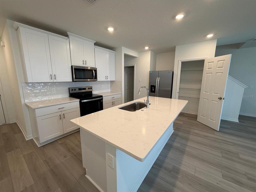 A kitchen features white cabinets, a central island with a sink, and stainless steel appliances — 4264 RANCH HOUSE ROAD, ST CLOUD, FL