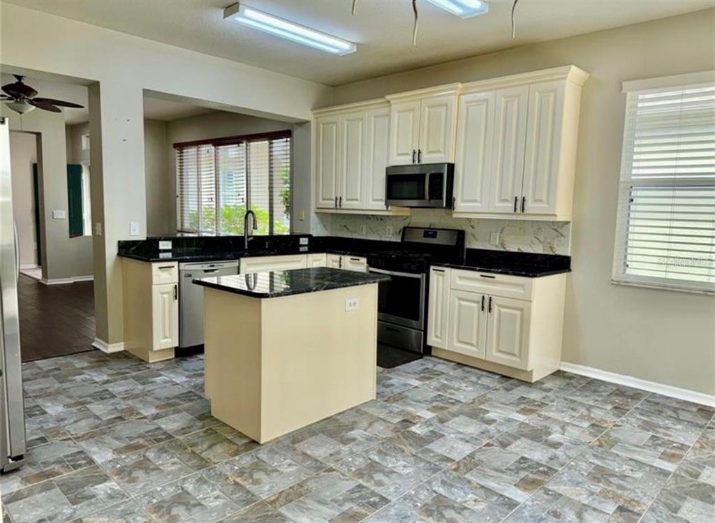 A kitchen features cream cabinets, black countertops, a center island, and gray tiled flooring — 30239 EMMETTS COURT, WESLEY CHAPEL, FL