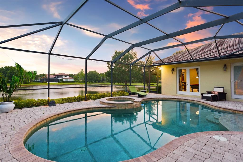 A screened-in pool and spa area with a brick paver deck overlooking a lake — 7906 FOXCATCHER COURT, ODESSA, FL