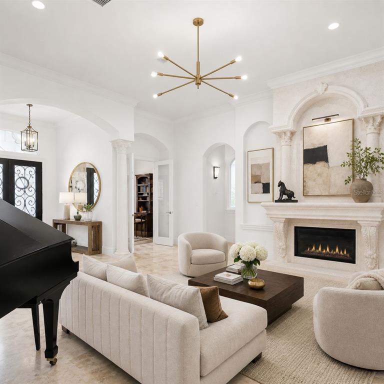 A bright living room features a grand piano, a fireplace, and a modern gold chandelier — 7906 FOXCATCHER COURT, ODESSA, FL