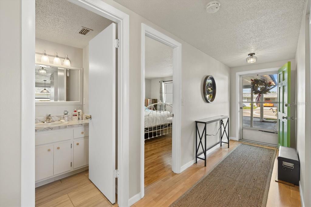 A hallway features light wood flooring, a console table, a round mirror, and white doors — 680 CIRCLEWOOD DRIVE UNIT W3, VENICE, FL