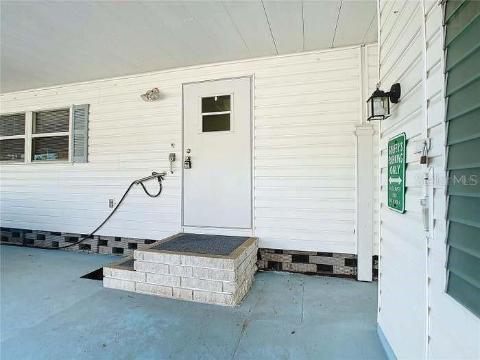 A white door with a small window sits above a brick step on a porch — 2331 BELLEAIR ROAD UNIT 116, CLEARWATER, FL