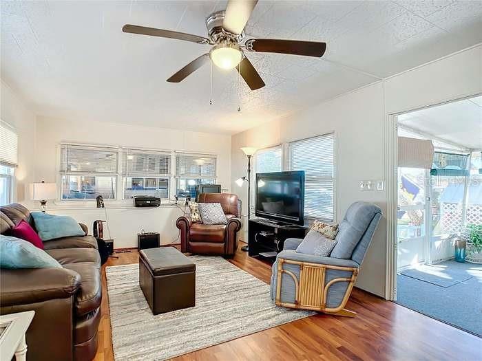 A living room features a ceiling fan, brown leather sofa, armchair, and a television console — 2331 BELLEAIR ROAD UNIT 116, CLEARWATER, FL