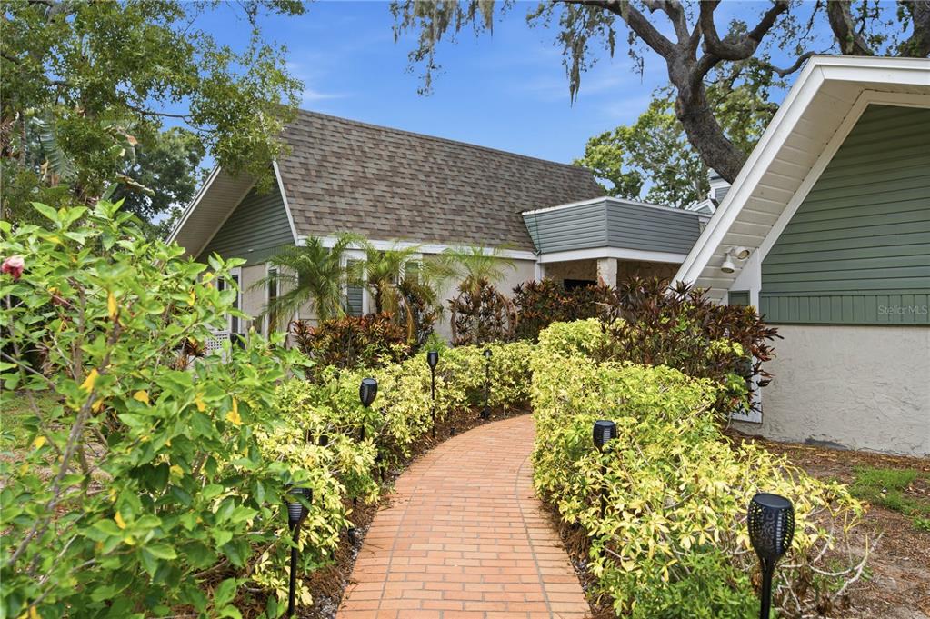 A brick walkway leads to the entrance of a house surrounded by lush green landscaping — 2860 BRIARWOOD LANE, PALM HARBOR, FL