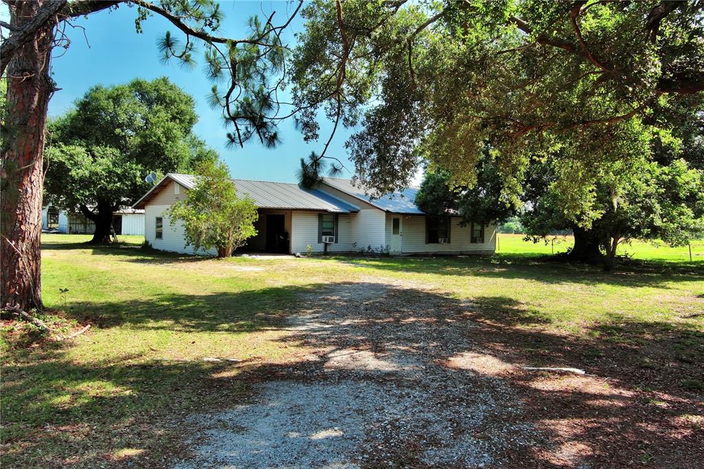 A single-story house with a metal roof sits on a gravel driveway under large trees — 15610 STATE ROAD 62, PARRISH, FL