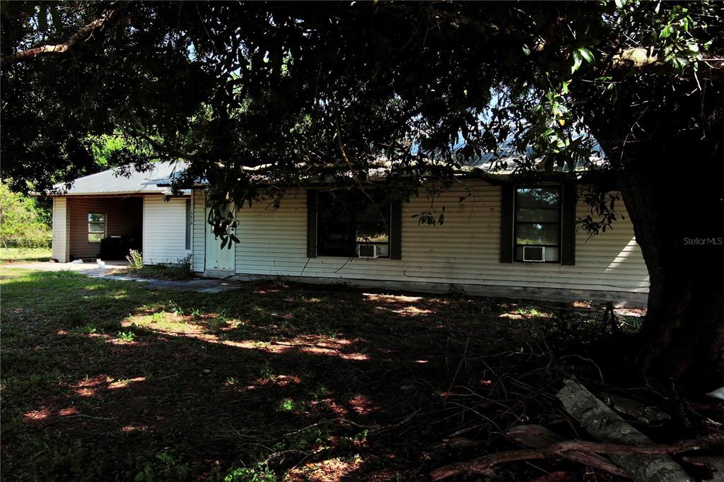 A single-story house with white siding and a carport sits under a large tree — 15610 STATE ROAD 62, PARRISH, FL