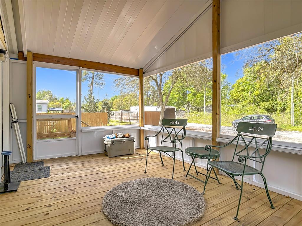 A screened-in porch with a wooden deck, two metal chairs, and a small table — 45750 PINE STREET, PAISLEY, FL