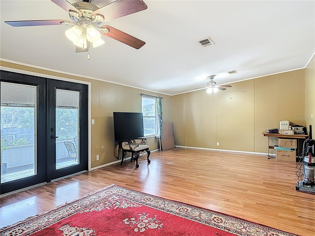 A living room with wood flooring, a ceiling fan, a television, and glass patio doors — 45750 PINE STREET, PAISLEY, FL
