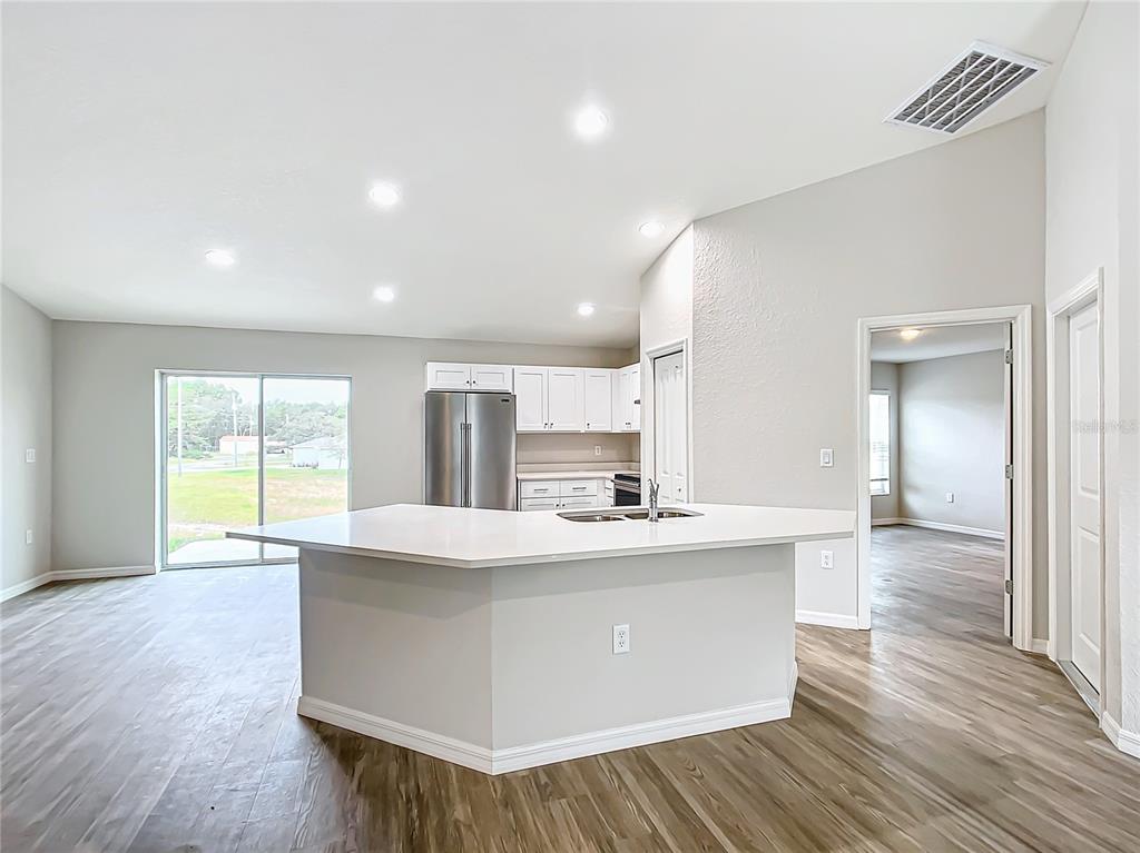 A kitchen with a white island, stainless steel refrigerator, and light wood-look flooring — 7850 SW 128TH STREET, OCALA, FL