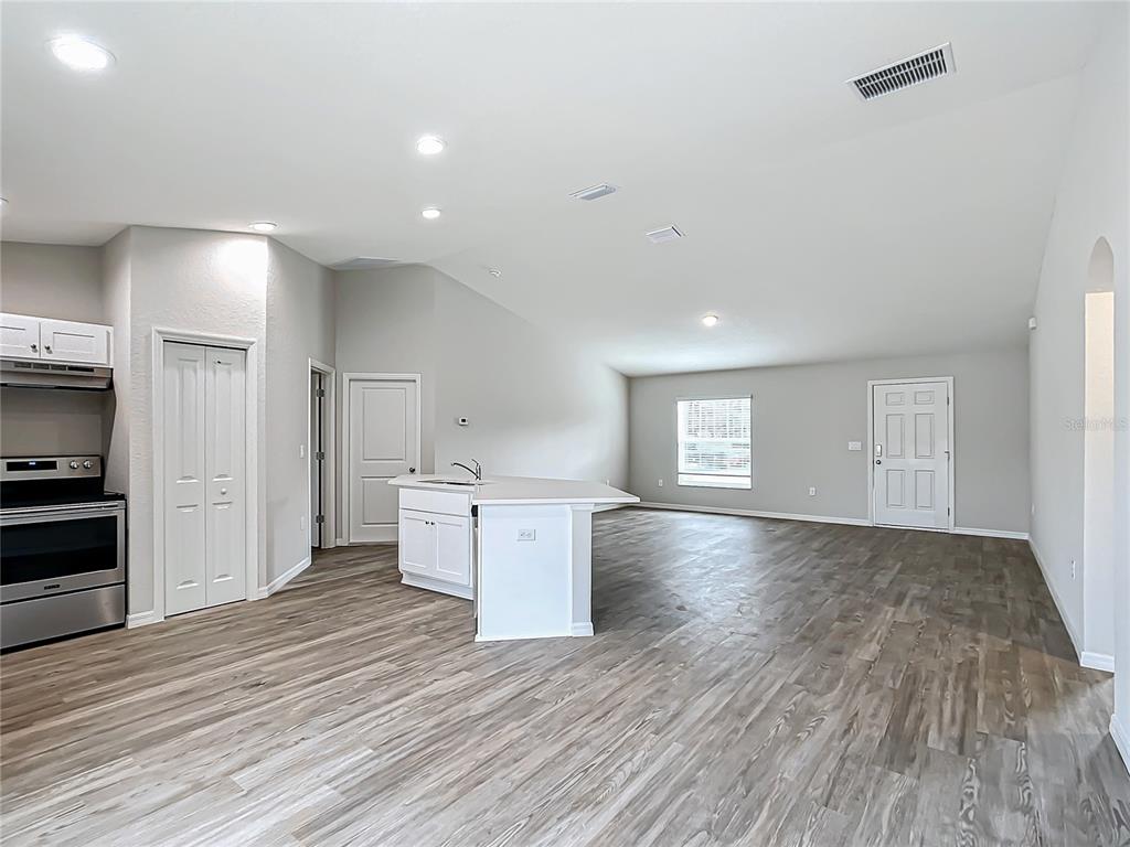 An open-concept kitchen and living area with white cabinets, a central island, and wood-look flooring — 7850 SW 128TH STREET, OCALA, FL