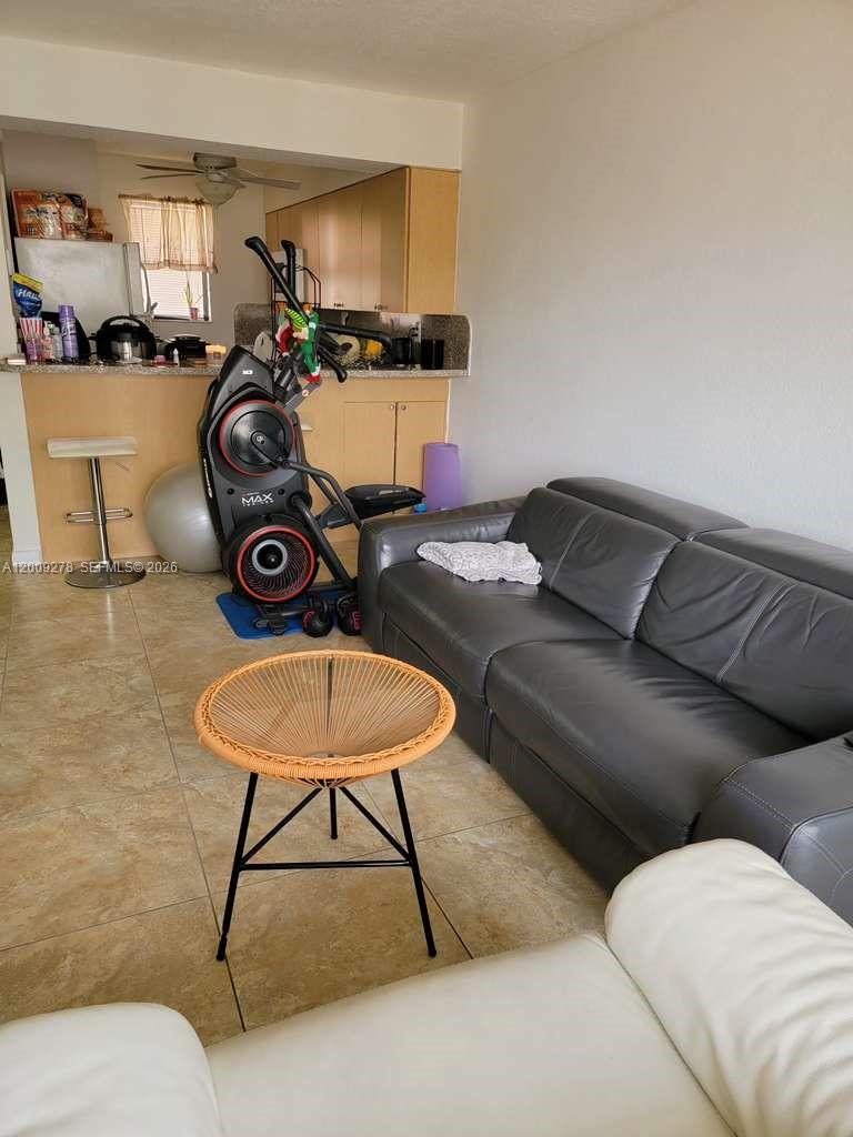 A living room features a grey leather sofa, a round woven coffee table, and an elliptical machine — 8425 NW 8th St # 306, Miami FL 33126, MIAMI, FL