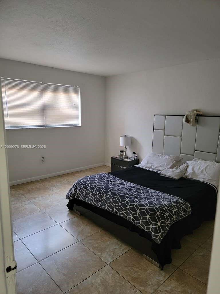 A bedroom features a bed with a geometric patterned cover, a headboard, and tile flooring — 8425 NW 8th St # 306, Miami FL 33126, MIAMI, FL