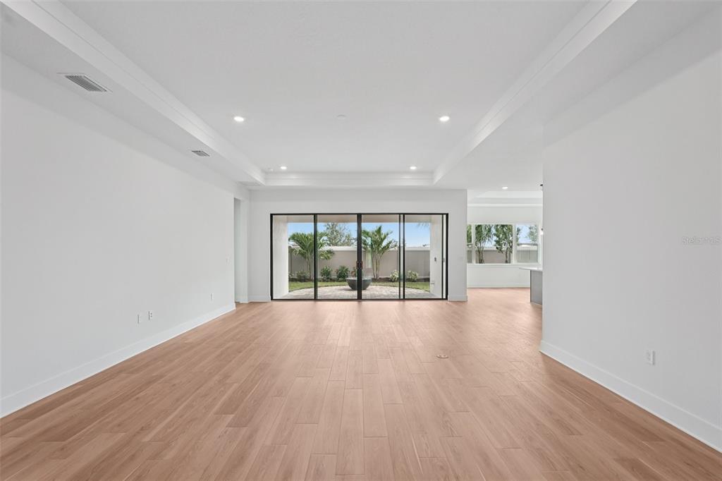 A spacious, empty living room features light wood-look flooring, white walls, and large sliding doors — 12652 IVORY TUSK LANE, SPRING HILL, FL