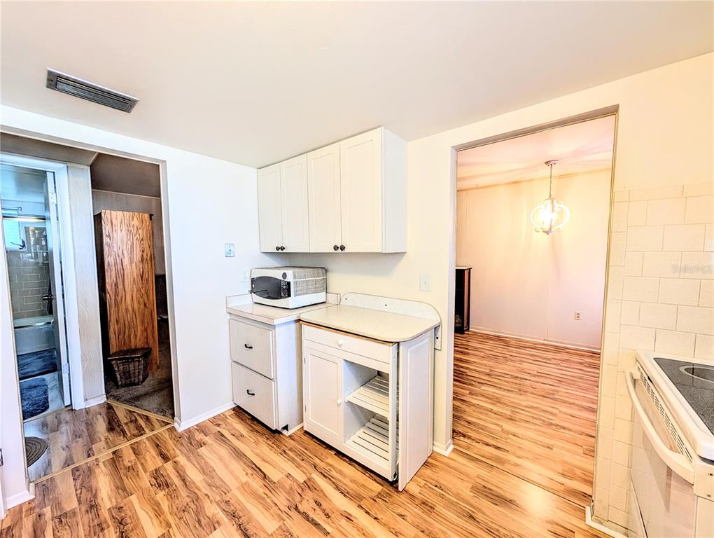 A kitchen with white cabinets, a microwave, and wood-look flooring, opening into an adjacent room — 5855 PALM LANE UNIT B21, BRADENTON, FL