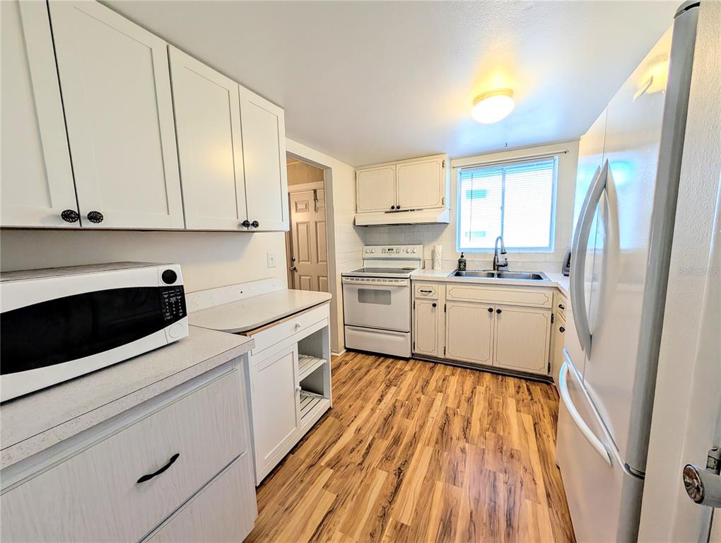 A kitchen with white cabinets, light countertops, white appliances, and wood-look flooring — 5855 PALM LANE UNIT B21, BRADENTON, FL