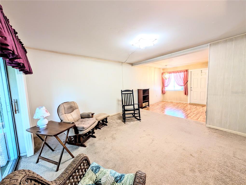 A living room with carpeted flooring connects to a dining area with wood-look flooring — 5855 PALM LANE UNIT B21, BRADENTON, FL