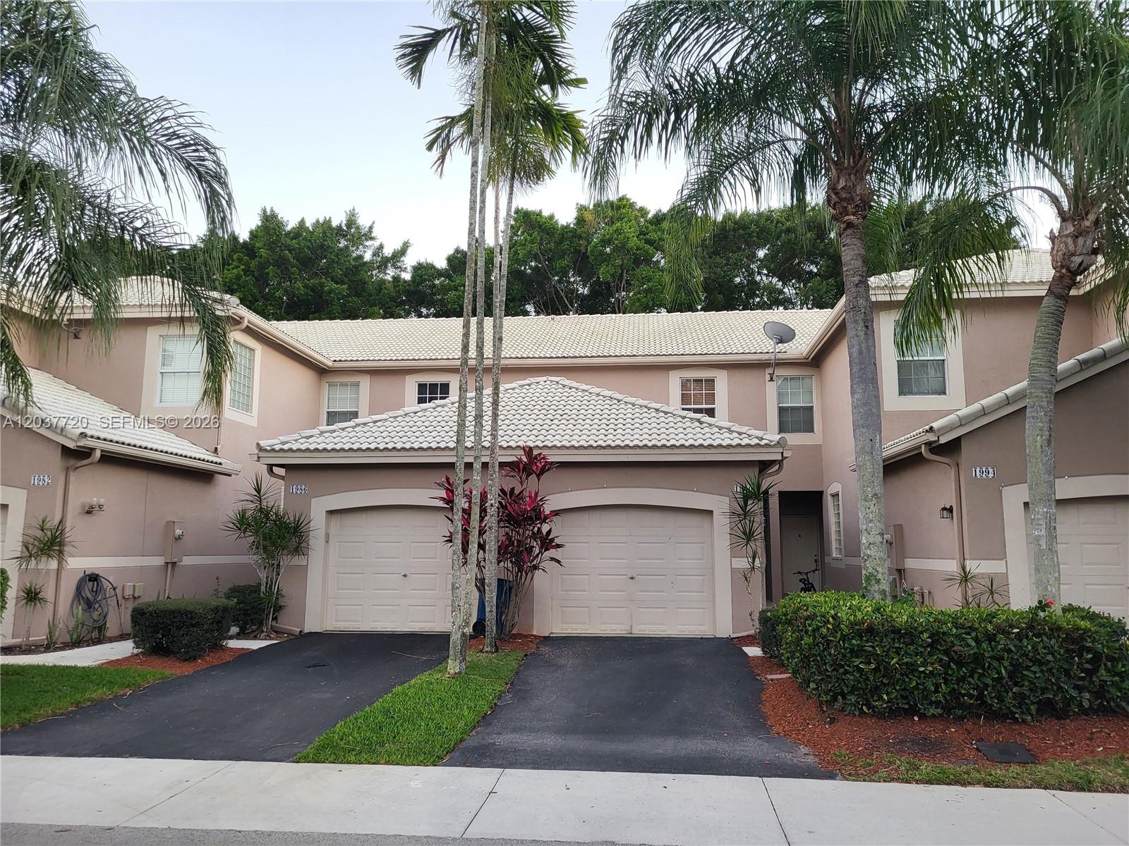 A two-story townhouse exterior features beige stucco walls, a light-colored tile roof, and two garages — 1990 Madeira Dr, Weston FL 33327, WESTON, FL