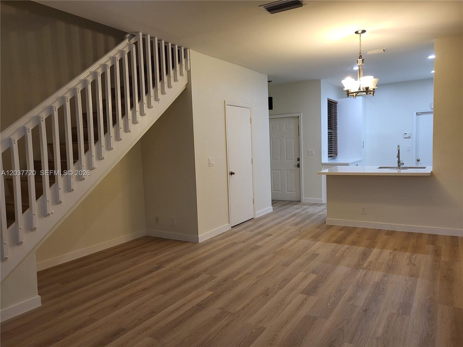An interior view shows a living area with wood-look flooring, a staircase, and a kitchen — 1990 Madeira Dr, Weston FL 33327, WESTON, FL