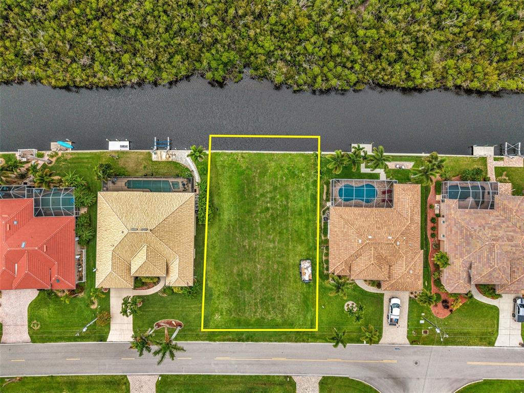 An aerial view shows a vacant residential lot situated between two houses along a canal — 645 MACEDONIA DRIVE, PUNTA GORDA, FL