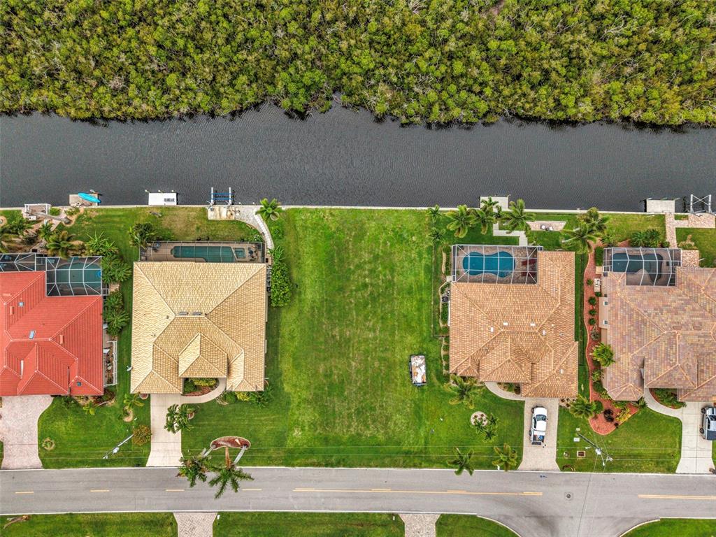An aerial view shows a vacant residential lot situated between two houses along a canal — 645 MACEDONIA DRIVE, PUNTA GORDA, FL