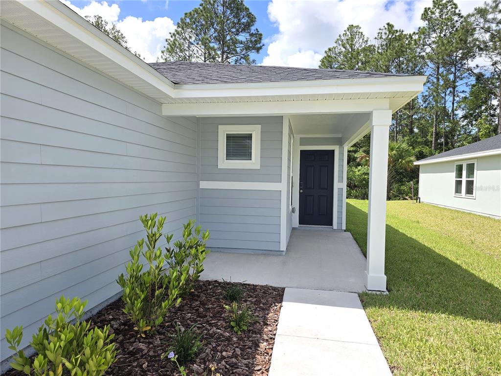 A light blue house exterior features a covered entryway, a dark door, and a walkway — 11 DILLY COURT, PALM COAST, FL