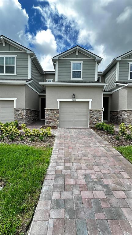A two-story townhouse exterior features a stone base, gray siding, and a paved driveway — 9040 OCEAN TIDE WAY, KISSIMMEE, FL