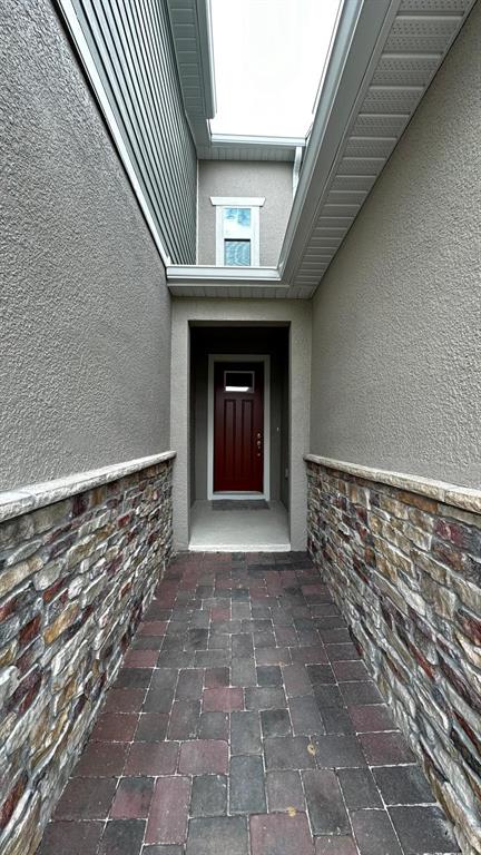 A narrow paved walkway leads to a red front door between stone-accented exterior walls — 9040 OCEAN TIDE WAY, KISSIMMEE, FL