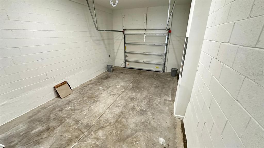 An empty garage features white painted block walls and a concrete floor — 9040 OCEAN TIDE WAY, KISSIMMEE, FL