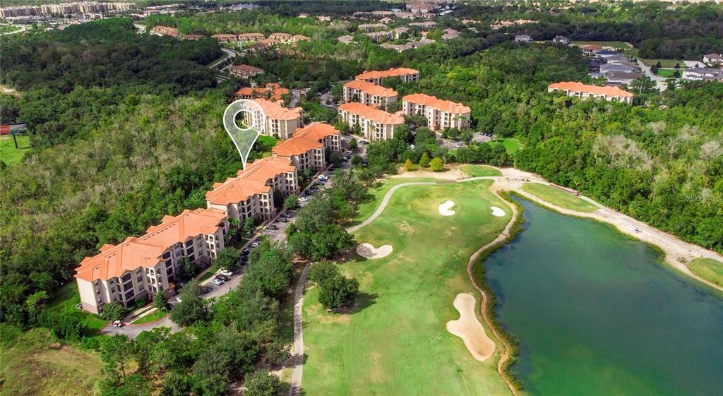 An aerial view shows a multi-story apartment complex situated next to a golf course and lake — 8010 TUSCANY WAY UNIT 5105, DAVENPORT, FL