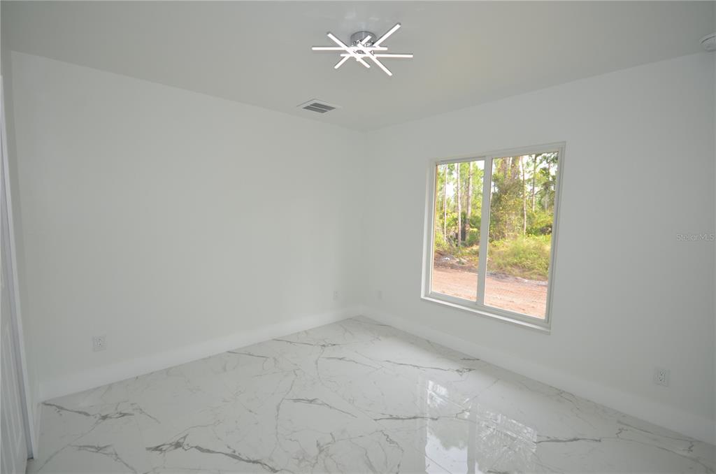 An empty room features white walls, marble-patterned tile flooring, a modern light fixture, and a window — 1132 EDELWEISS STREET E, LEHIGH ACRES, FL