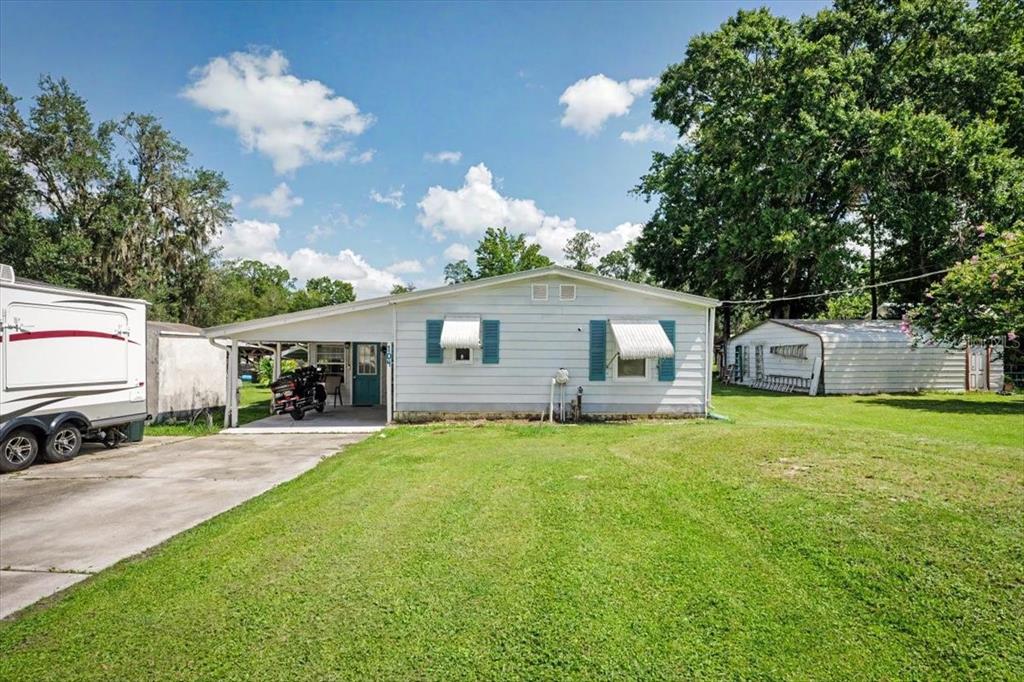 A single-story house with white siding, blue shutters, and a carport on a grassy lot — 104 EDGEWATER ROAD, SATSUMA, FL