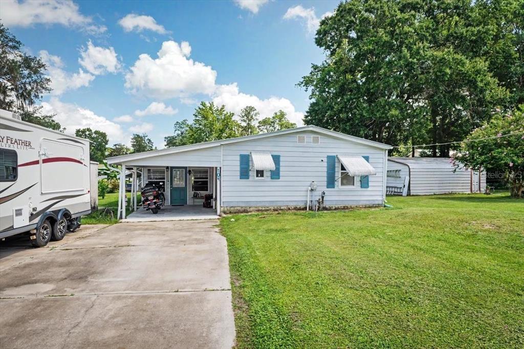 A single-story house with a carport, blue shutters, and a concrete driveway on a lawn — 104 EDGEWATER ROAD, SATSUMA, FL