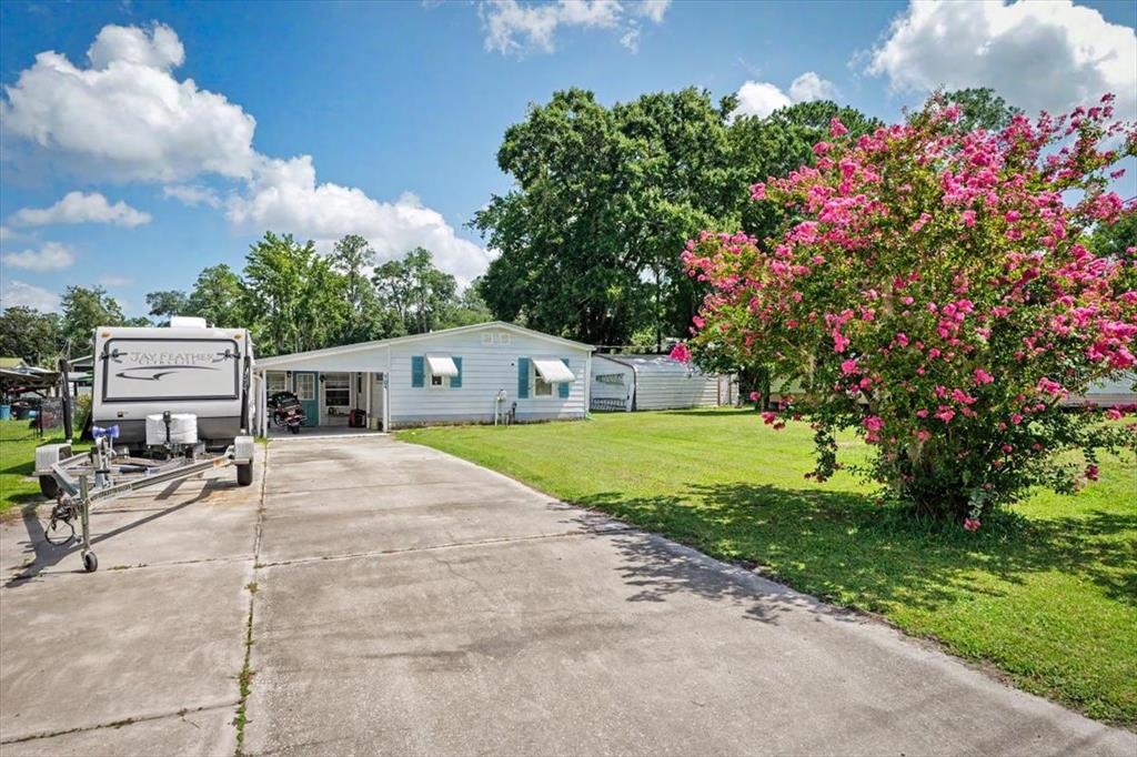 A single-story house with a concrete driveway, a parked travel trailer, and a blooming tree — 104 EDGEWATER ROAD, SATSUMA, FL
