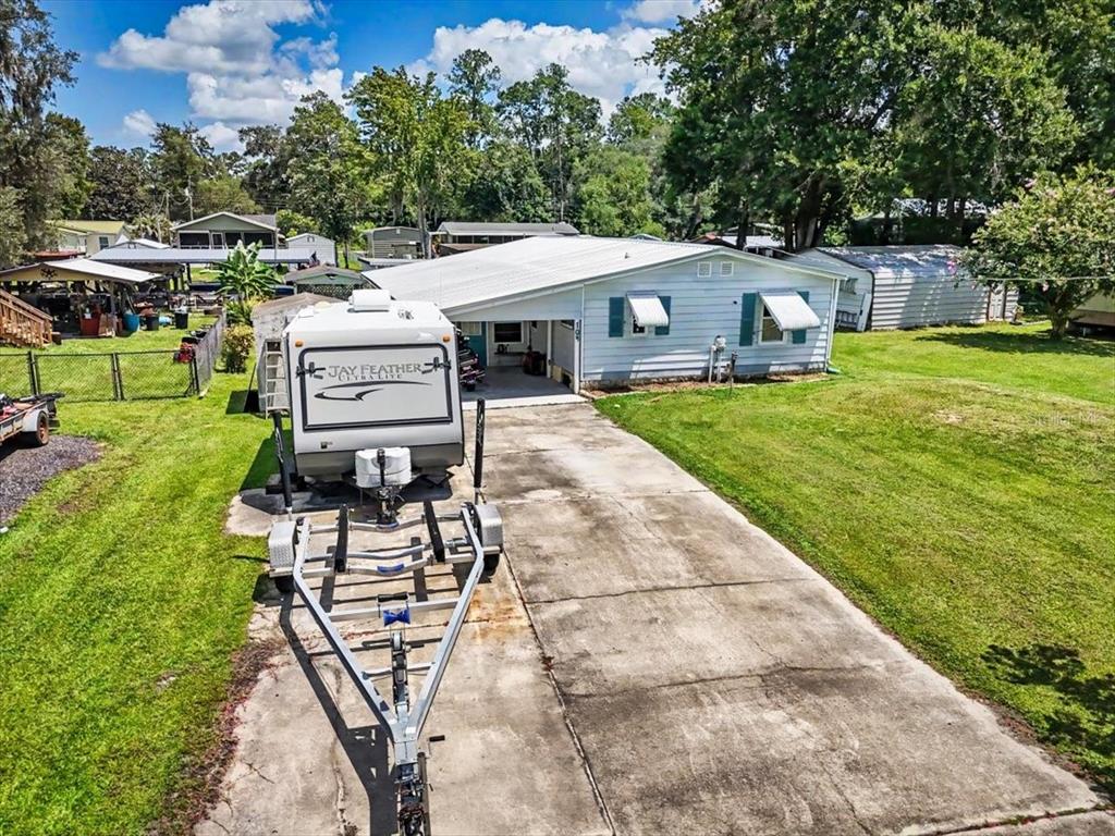 A single-story house with a concrete driveway, a parked travel trailer, and a blooming tree — 104 EDGEWATER ROAD, SATSUMA, FL