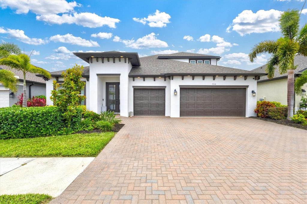 A modern single-story house with a white exterior, dark garage doors, and a paved driveway — 5516 NORTHERN JUNIPER COURT, SARASOTA, FL