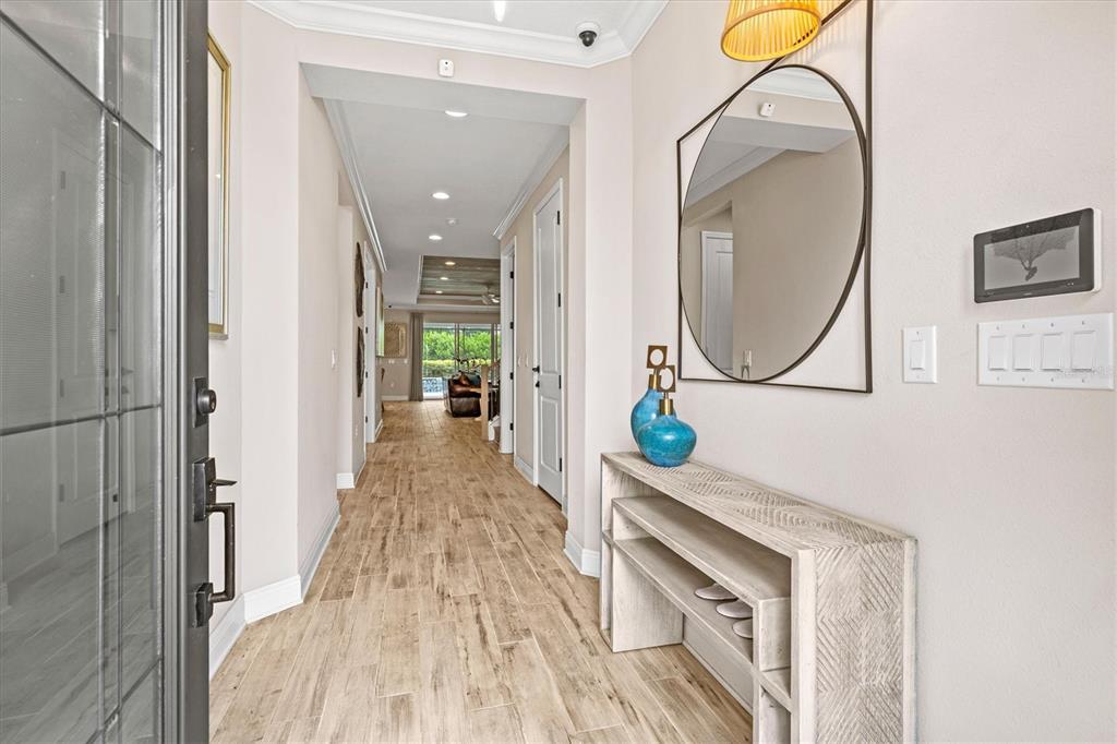 A bright entryway features wood-look tile flooring, a console table, and a circular wall mirror — 5516 NORTHERN JUNIPER COURT, SARASOTA, FL