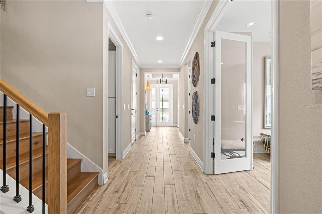 A hallway with light wood-look tile floors, a wooden staircase, and a glass-paneled door — 5516 NORTHERN JUNIPER COURT, SARASOTA, FL