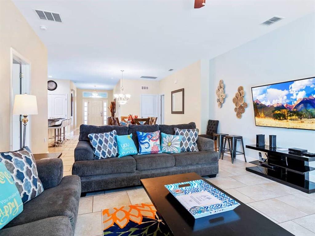 A living room features a dark gray sofa, a coffee table, and a wall-mounted television — 4408 ACORN COURT, DAVENPORT, FL