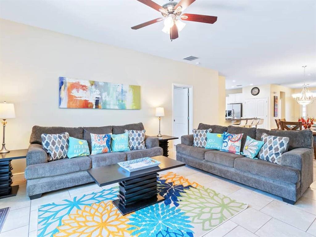 A living room features two gray sofas, a patterned area rug, and a ceiling fan — 4408 ACORN COURT, DAVENPORT, FL