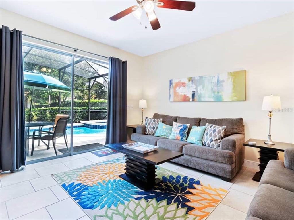 A living room with a gray sofa, patterned rug, and sliding doors opening to a pool — 4408 ACORN COURT, DAVENPORT, FL