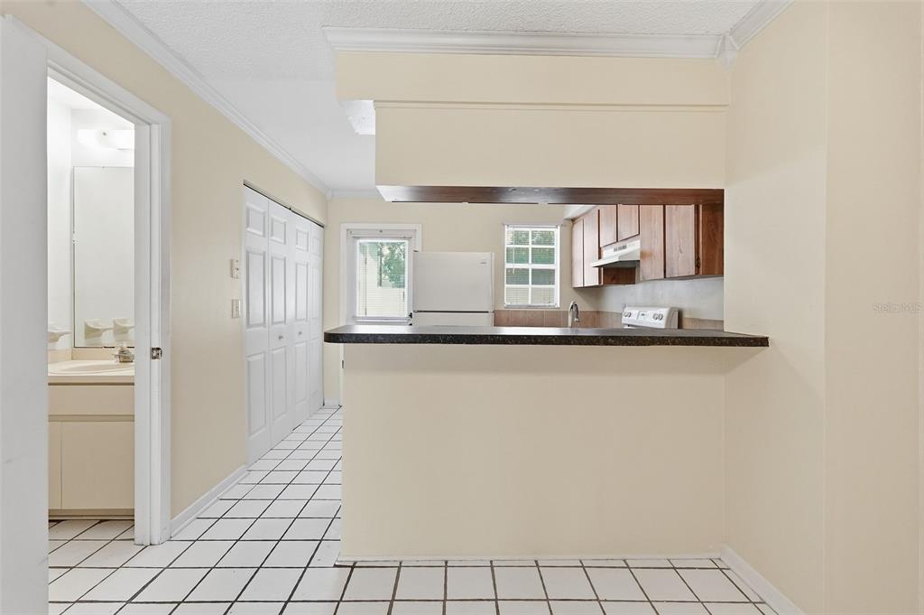 A kitchen with a breakfast bar, white appliances, and wood cabinets overlooks a tiled hallway — 6620 121ST AVENUE UNIT 1, LARGO, FL