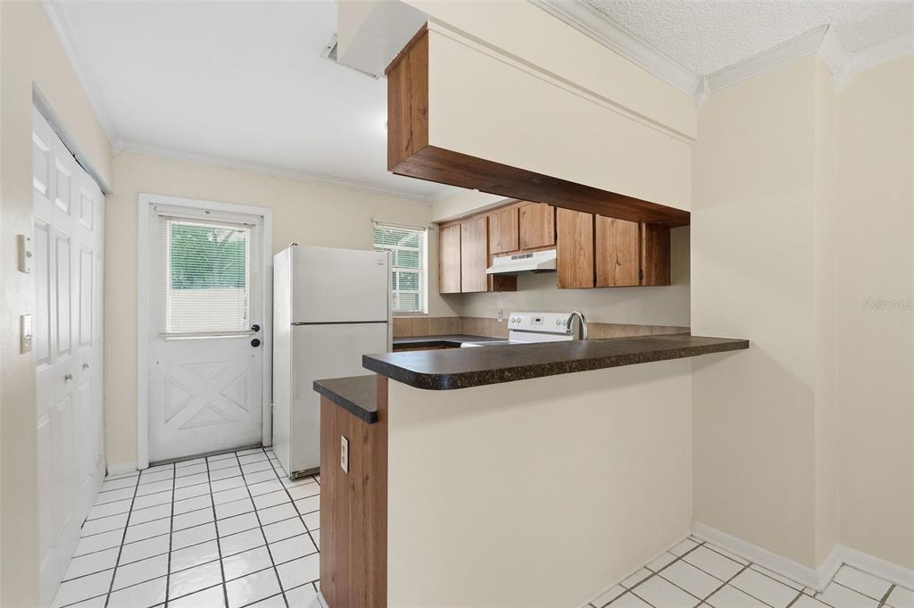 A kitchen features a breakfast bar, white appliances, wood cabinets, and white tiled flooring — 6620 121ST AVENUE UNIT 1, LARGO, FL