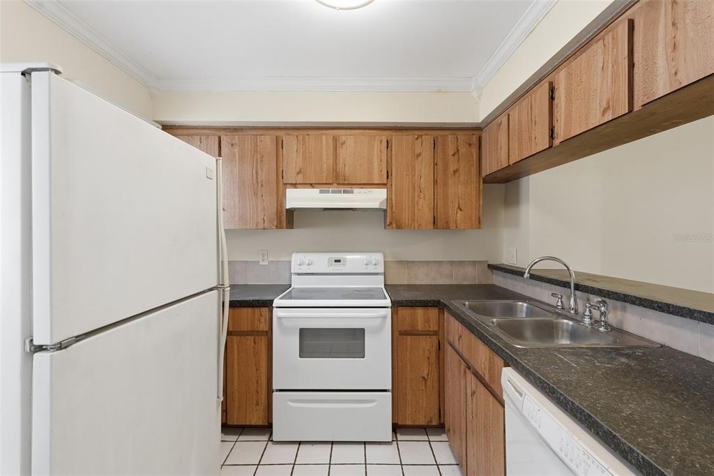 A kitchen features wood cabinets, white appliances, dark countertops, and white tile flooring — 6620 121ST AVENUE UNIT 1, LARGO, FL