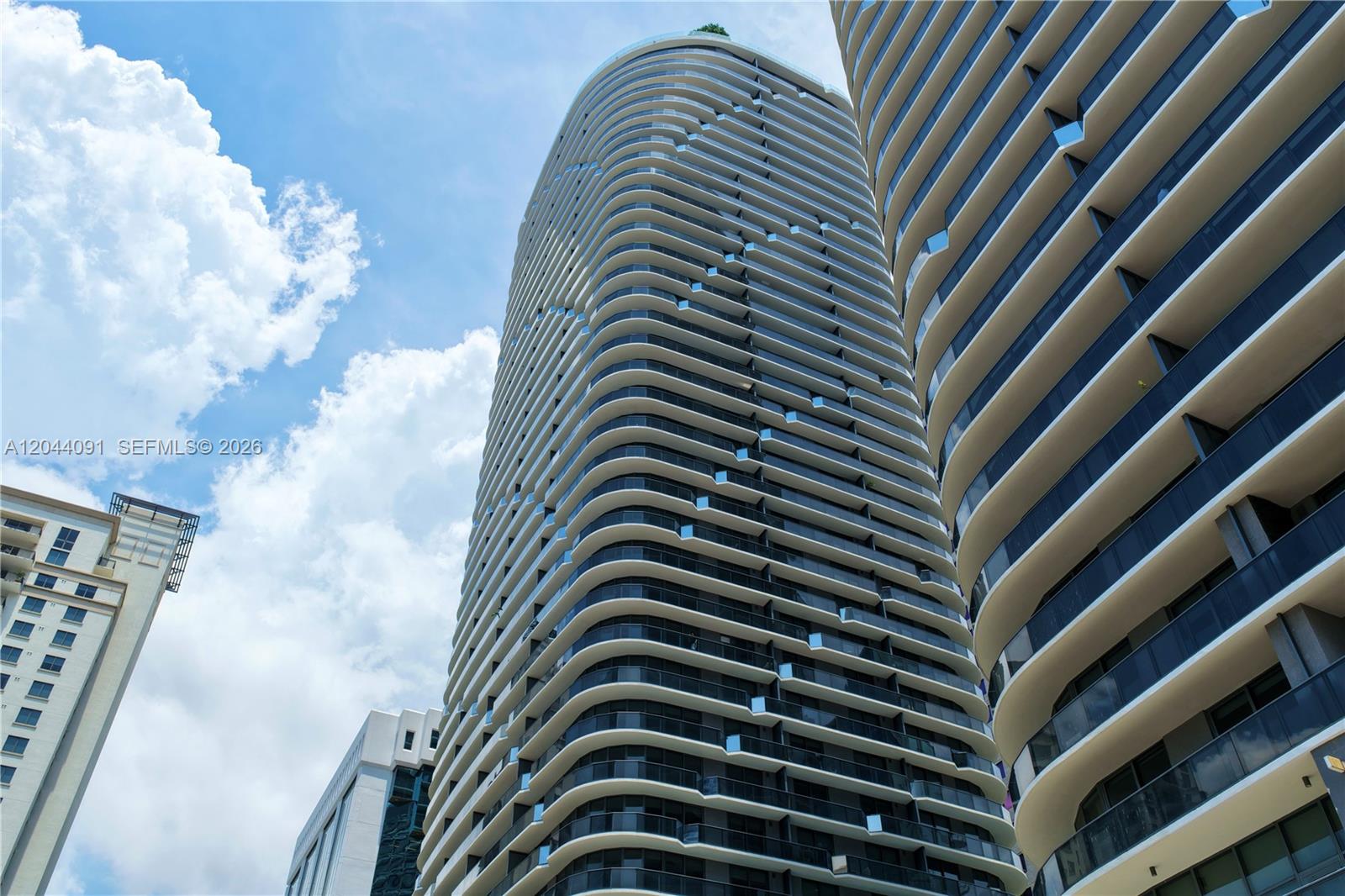 Low-angle view of two modern, curved high-rise residential towers against a blue sky — 55 SW 9th St # 2208, Miami FL 33130, MIAMI, FL