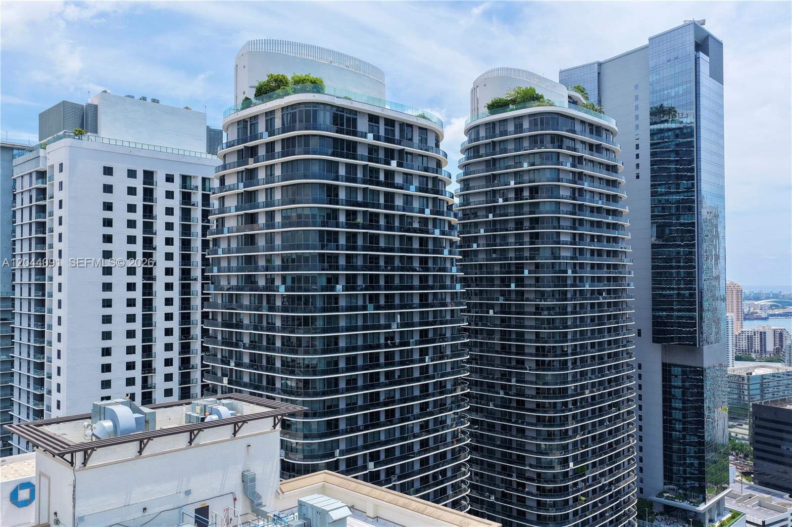 An exterior view shows two modern curved residential towers with balconies and rooftop gardens — 55 SW 9th St # 2208, Miami FL 33130, MIAMI, FL