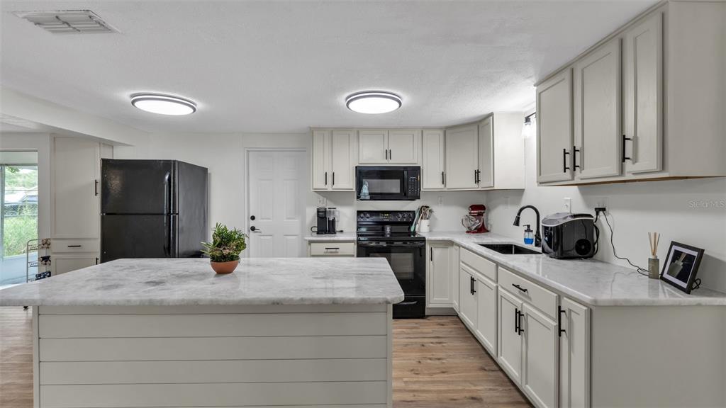A kitchen features white cabinets, marble countertops, a central island, and black appliances — 217 4TH JPV STREET, WINTER HAVEN, FL