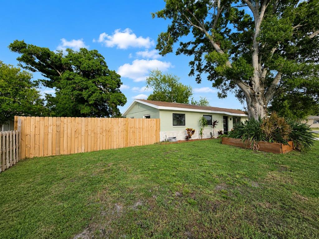 A light green house with a wooden fence and a large tree in the yard — 7001 59TH STREET N, PINELLAS PARK, FL