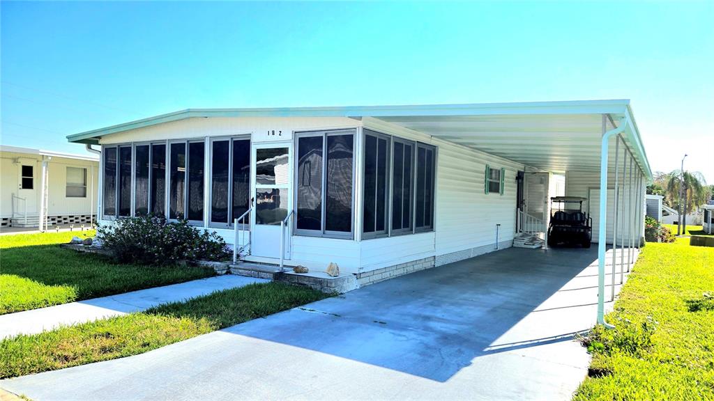 A white mobile home features a screened-in front porch and an attached covered carport — 39820 US HIGHWAY 19 N UNIT 182, TARPON SPRINGS, FL