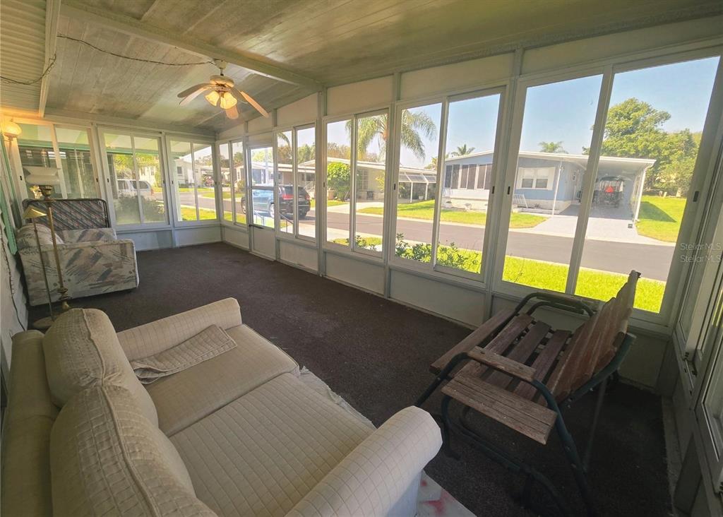 A sunroom with a ceiling fan, carpeted floor, and large windows overlooking a residential street — 39820 US HIGHWAY 19 N UNIT 182, TARPON SPRINGS, FL